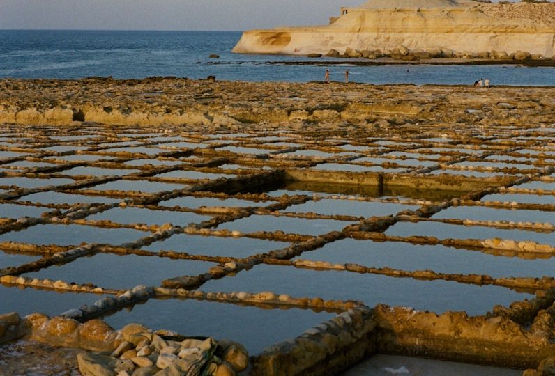 Salt pans by the ocean with distant rocky hills.